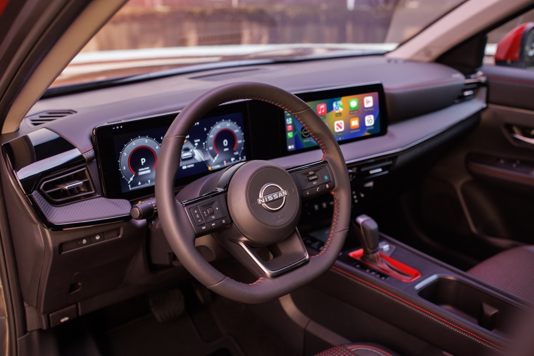 Vue intérieure du Nissan Kicks 2025 SR montrant le volant, les écrans numériques et les surpiqûres rouges sur le tableau de bord.