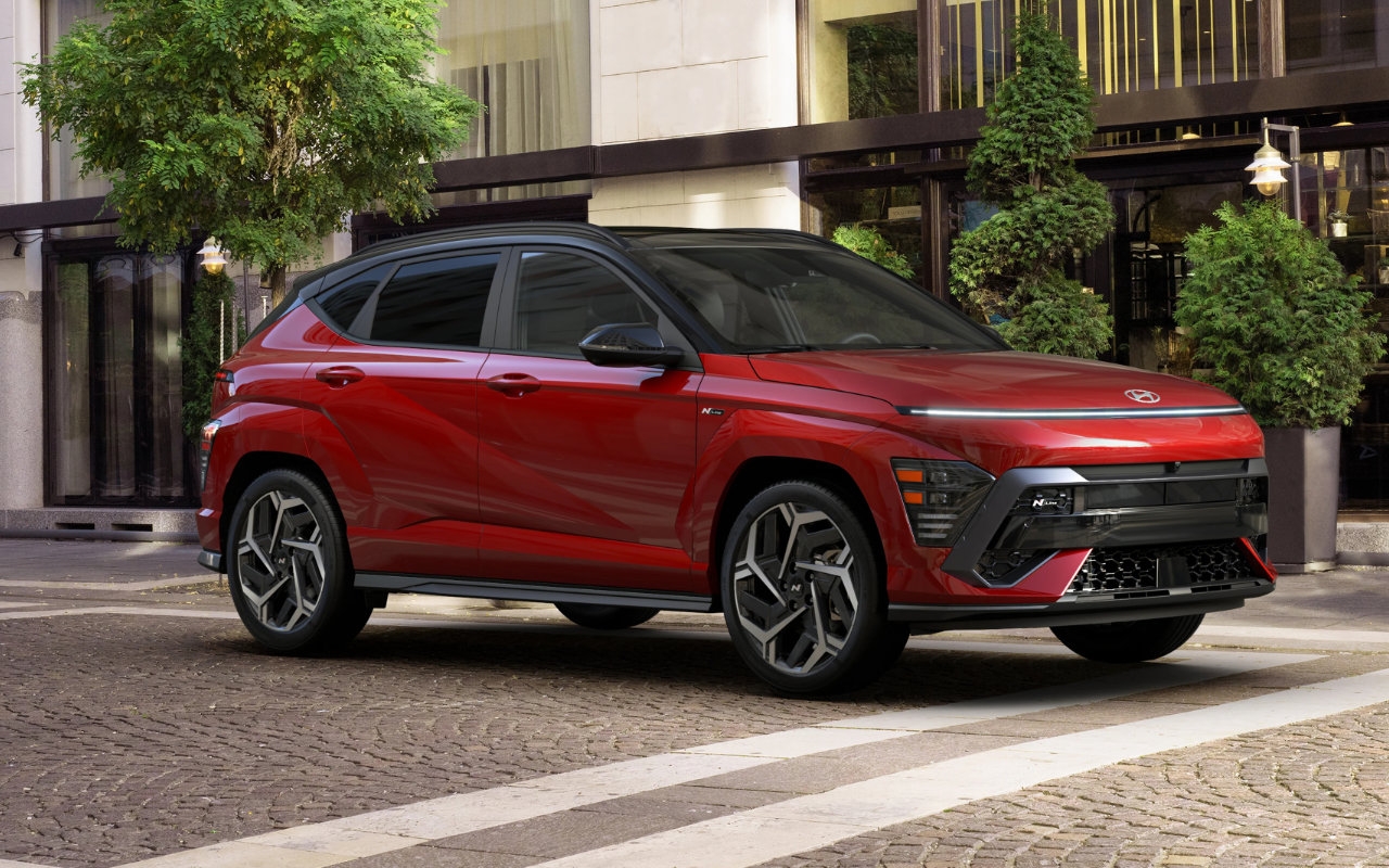 Vue trois quarts avant du Hyundai Kona 2025 rouge stationné en ville, mettant en valeur son design sportif et ses jantes noires bicolores.