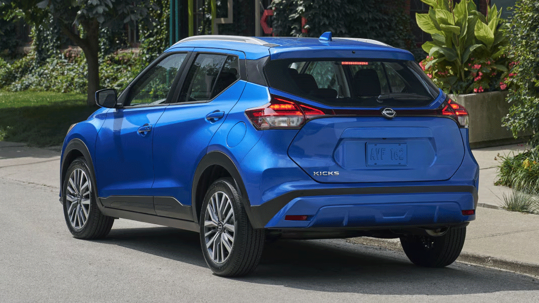 Vue arrière du Nissan Kicks Play 2025, garé en bord de route devant une maison avec arbres et plantes