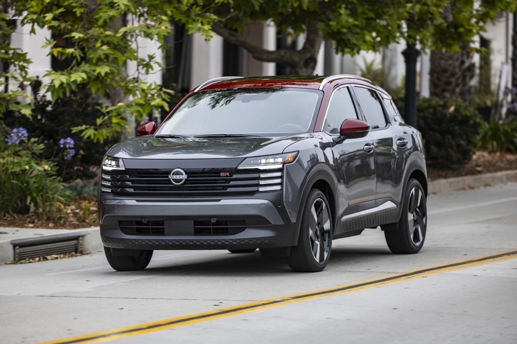 Nissan Kicks 2026 gris SR en mouvement sur rue urbaine bordée d’arbres, un VUS sous-compact moderne, dynamique et abordable.