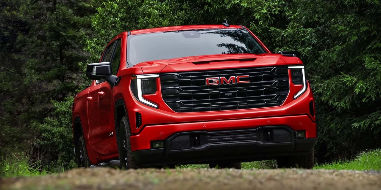 GMC Sierra 1500 2026 rouge en vue avant dans une forêt dense, éclairé par une lumière naturelle douce.