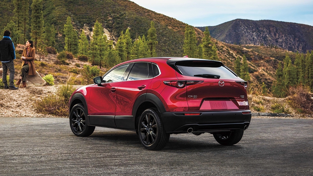 Vue arrière trois quarts du Mazda CX-30 2025 rouge sur route de montagne, soulignant ses lignes élégantes et son allure dynamique.